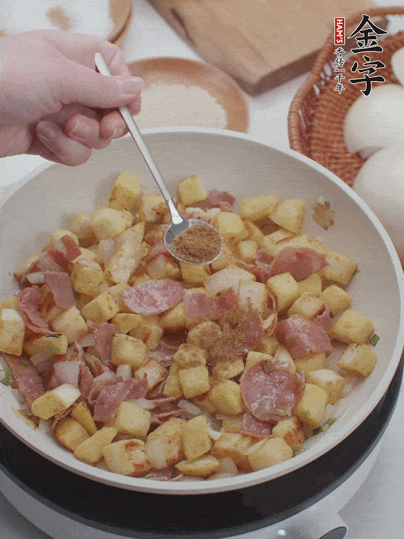 起鍋少油，煸香洋蔥丁、蔥白，加入金字培根火腿翻炒幾下，再加入饅頭丁、1小勺孜然粉、少許鹽翻炒均勻并鋪平。